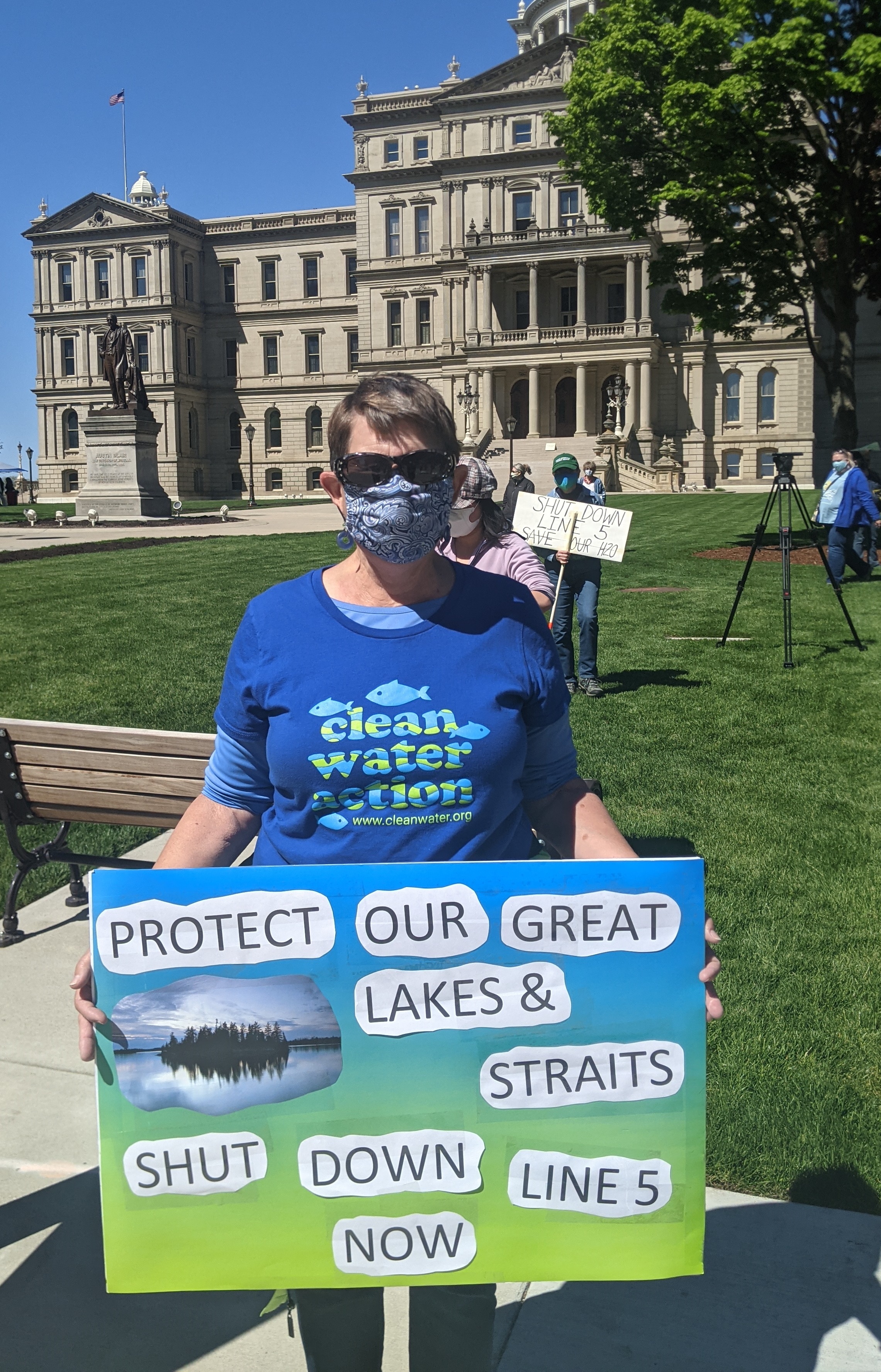 Protestor holding sign saying: "Protect Our Great Lakes & Straits, Shut Down Line 5 Now" in front of the MI state capitol building
