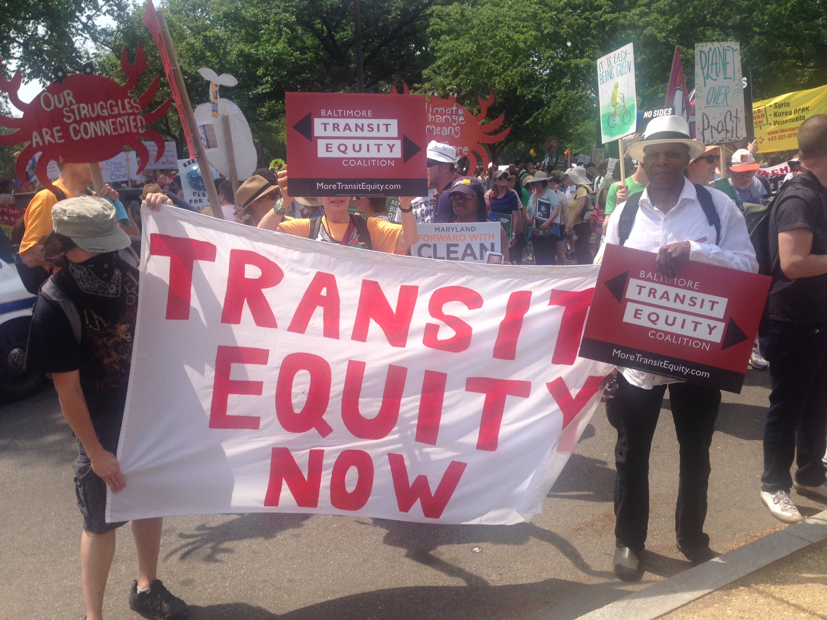 Supporters of the Baltimore Transit Equity Coalition hold a sign at the 2017 Peoples Climate March that reads "Transit Equity Now" Supporters of the Baltimore Transit Equity Coalition hold a sign at the 2017 Peoples Climate March that reads "Transit Equity Now"